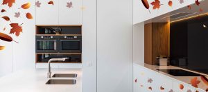 luxe op maat gemaakte keuken van wit fineer met eiken houten details en ingebouwd keukenapparatuur. De afbeelding bevat in de hoek als grafisch element geïllustreerde herfstbladeren