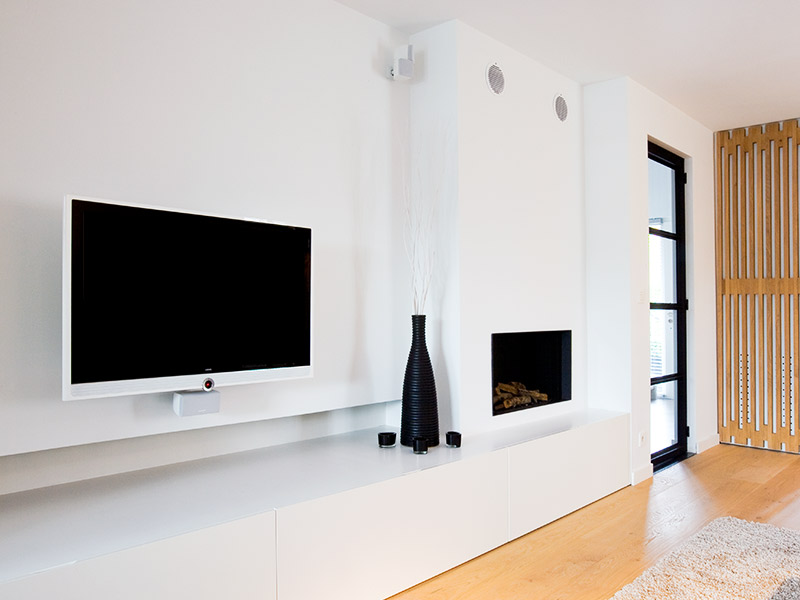 flatscreen televisie tegen de muur met een witte dressoir eronder, ingebouwde speakers in de muur en een wit haardmeubel