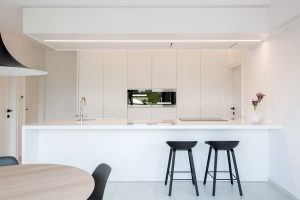 Totaalproject, keukentafel en twee zwarte barstoelen aan het keukeneiland met zicht op witte inbouwkasten